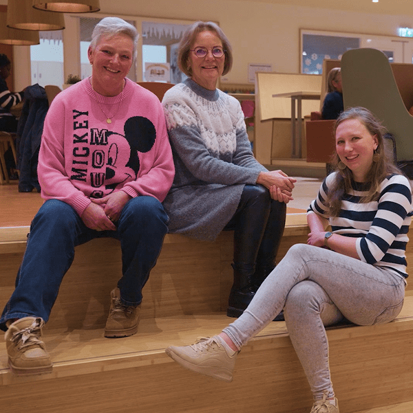 Drie vrouwelijke medewerkers van de Kinderkoepel poseren op een houten trap