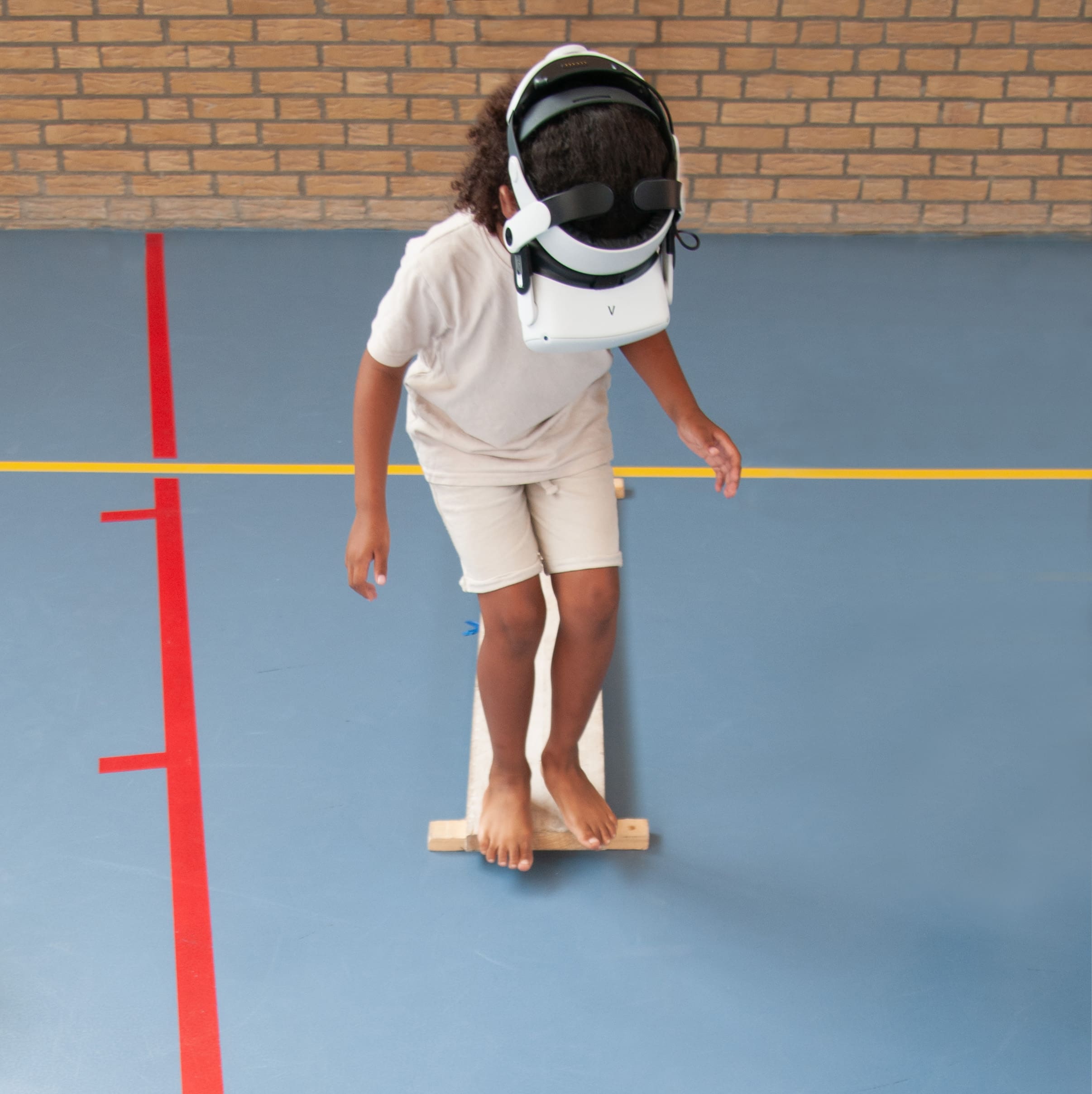 Kind met VR-bril balanceert op houten plank tijdens evenwichtstraining in gymnastiekzaal
